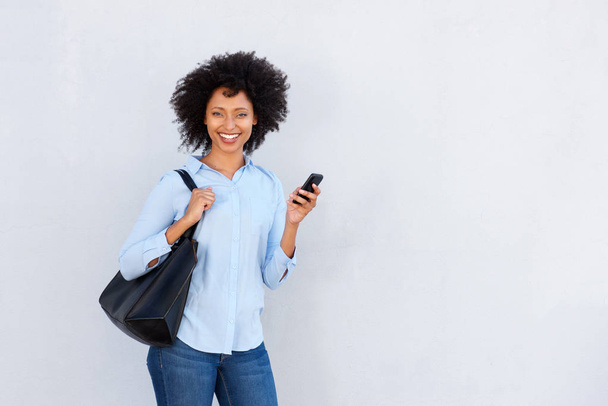 Портрет впевненої молодої чорної жінки, що тримає мобільний телефон і посміхається на білому тлі
 - Фото, зображення