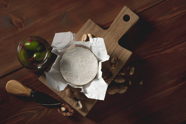 flat lay with brie cheese, knife, herbs and jars with olives and capperi on wooden table - Photo, image