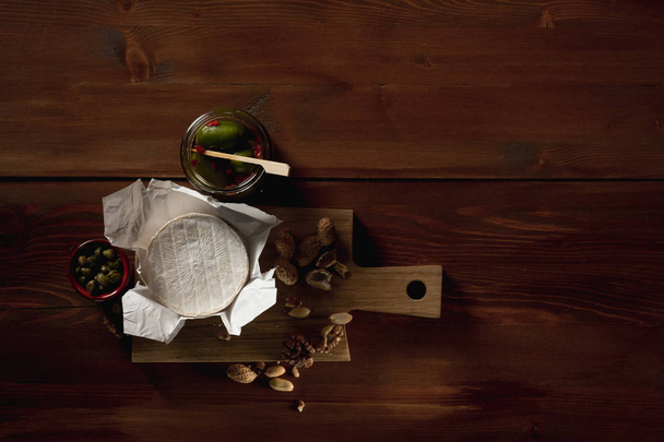 flat lay with brie cheese, knife, herbs and jars with olives and capperi on wooden table - Fotografie, Obrázek
