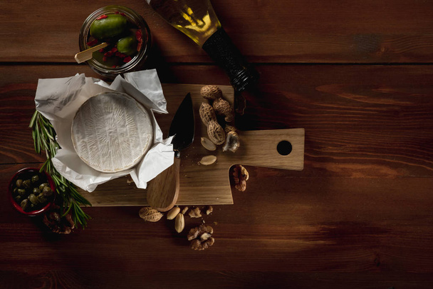 flat lay with brie cheese, knife, herbs and jars with olives and capperi on wooden table - Фото, зображення