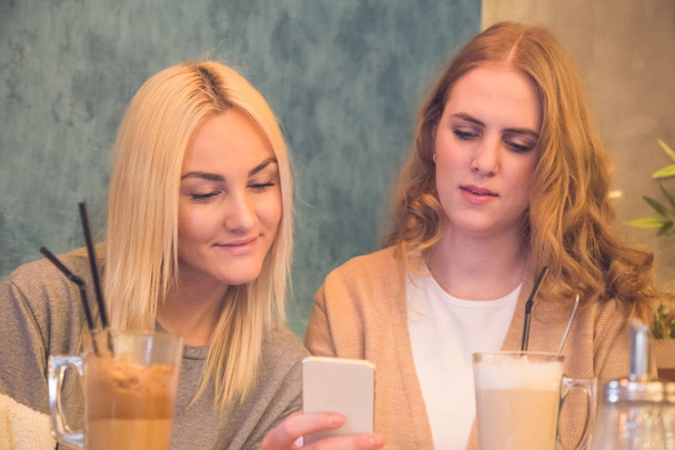 Nahaufnahme von zwei Mädchen, die ihr Handy im Café benutzen und trinken - Foto, Bild