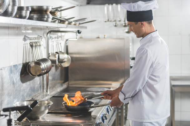 イケメン シェフのステーキ レストランのキッチンで火をフライパンの側面図 - 写真・画像