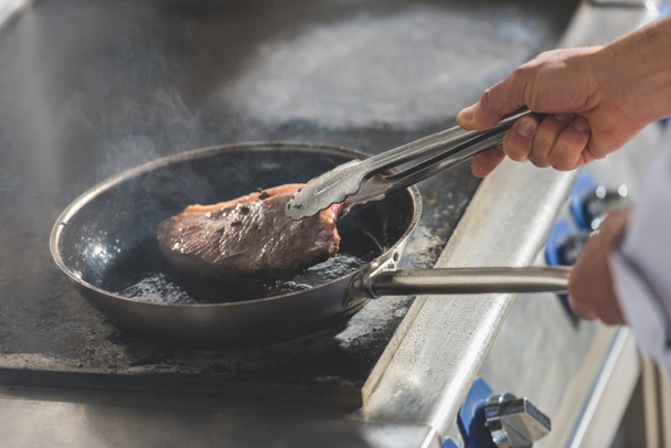 cropped image of chef frying steak at restaurant kitchen - Valokuva, kuva