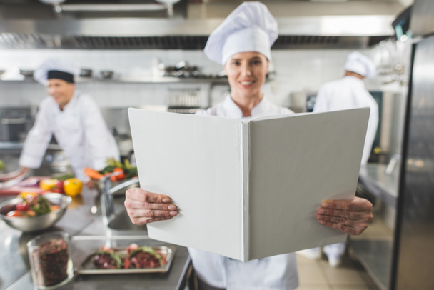 χαμογελώντας σεφ, κρατώντας το βιβλίο συνταγών στην κουζίνα εστιατορίου - Φωτογραφία, εικόνα