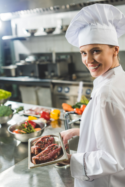 attractive chef holding tray with raw meat at restaurant kitchen - Foto, Imagen