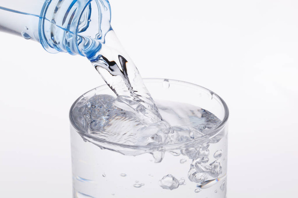 Despejar água da garrafa em vidro sobre fundo branco. - Foto, Imagem