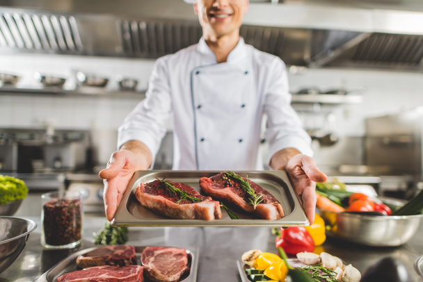 cropped image of chef holding tray with raw steaks at restaurant kitchen - Fotografie, Obrázek