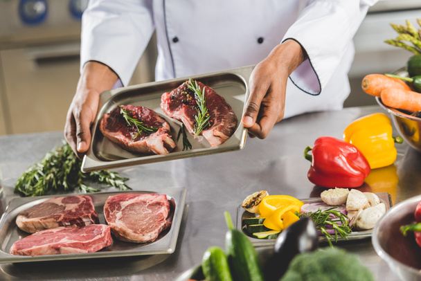 cropped image of african american chef holding tray with raw meat at restaurant kitchen  - Photo, Image