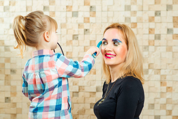 Cute little girl are doing funny make up to her mother. - Fotó, kép
