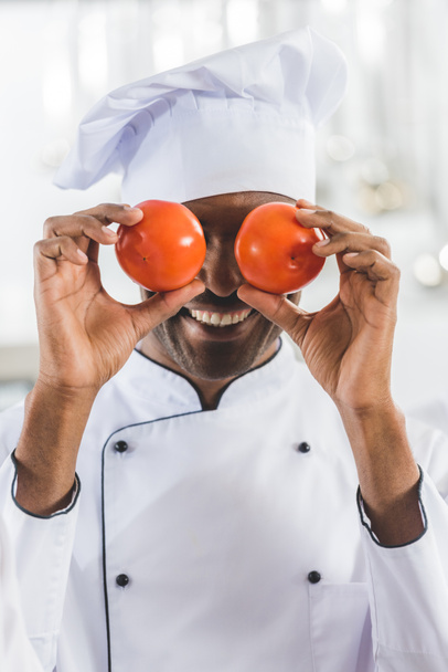 handsome african american chef covering eyes with tomatoes at restaurant kitchen - Photo, Image