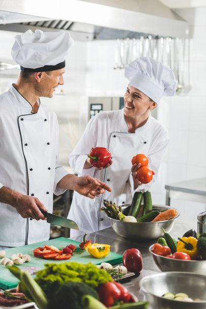 glimlachend chef-koks koken en bij elkaar kijken naar restaurant keuken - Foto, afbeelding