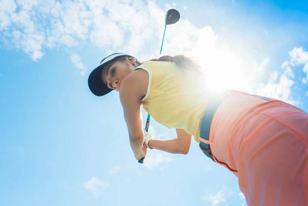 Vista de bajo ángulo de una jugadora profesional que sostiene el palo de hierro con concentración para la huelga mientras juega al golf al aire libre contra el cielo nublado
 - Foto, Imagen