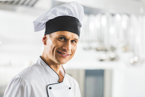 портрет улыбающегося красивого шеф-повара, смотрящего в камеру на кухне ресторана
 - Фото, изображение