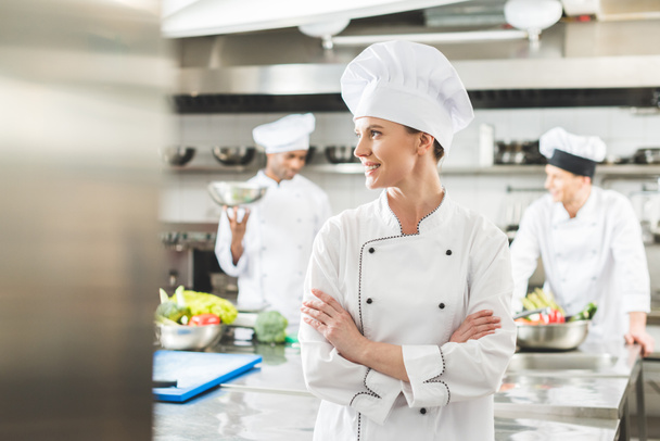 chef sonriente de pie con los brazos cruzados y mirando hacia la cocina del restaurante
 - Foto, imagen
