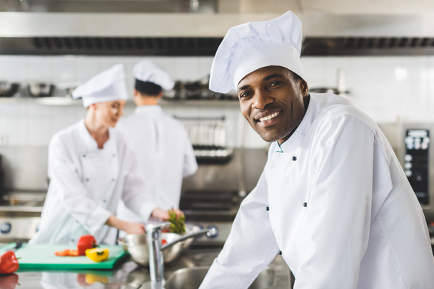 smiling african american chef looking at camera at restaurant kitchen - Foto, imagen