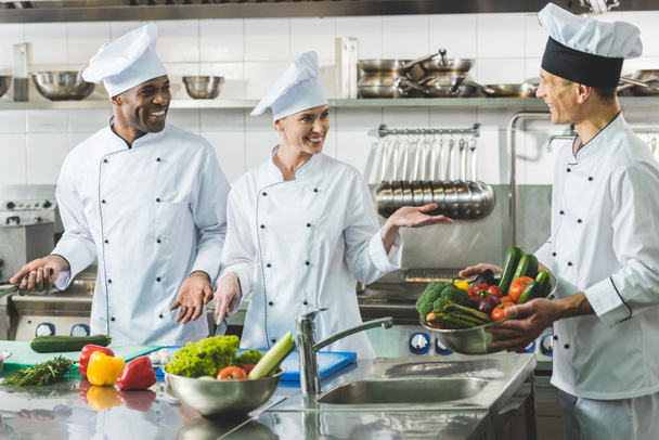 smiling multicultural chefs talking at restaurant kitchen - Foto, Bild