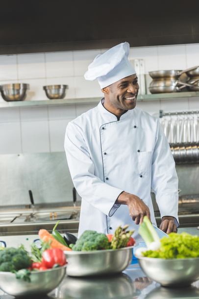 レストランのキッチンで笑顔のハンサムなアフリカ系アメリカ人シェフ カット野菜 - 写真・画像