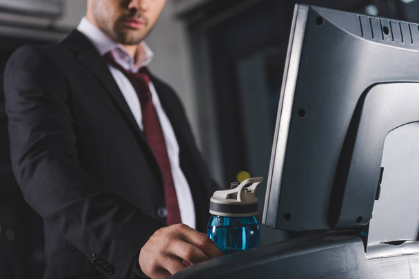 cropped view of businessman training on treadmill and taking sport bottle in gym - Photo, Image