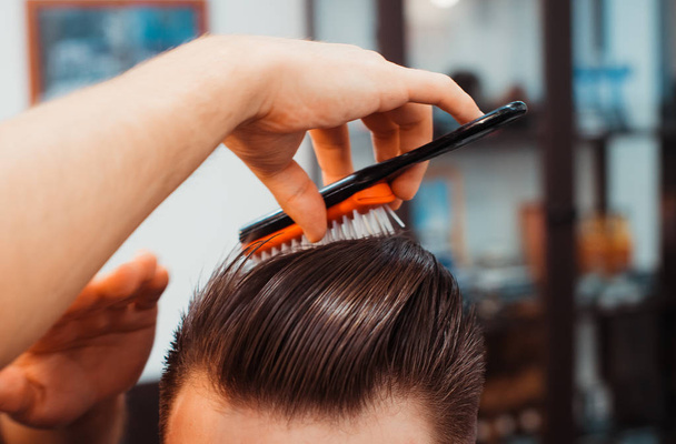 Мастер стрижет волосы и бороду мужчин в парикмахерской, парикмахер делает прическу для молодого человека
 - Фото, изображение