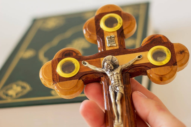       χέρι που κρατά ένα σταυρό παριστάνει τη σταύρωση του Ιησού Χριστού φόντο την Αγία Γραφή - Φωτογραφία, εικόνα