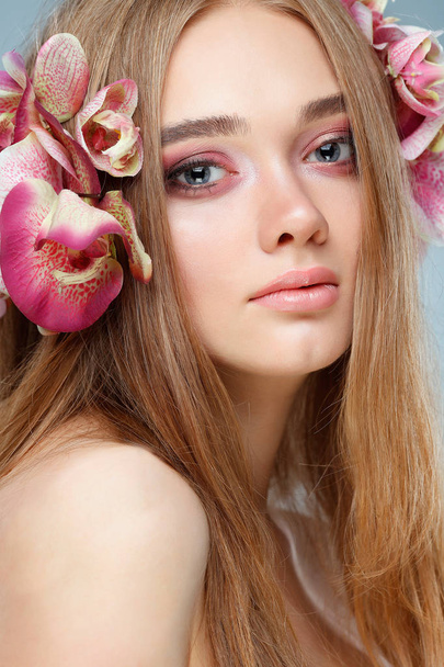 Beautiful girl, isolated on a light - violet  background with varicoloured flowers in hairs, emotions, cosmetics - Foto, imagen