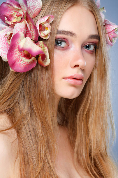 Beautiful girl, isolated on a light - violet  background with varicoloured flowers in hairs, emotions, cosmetics - Foto, imagen