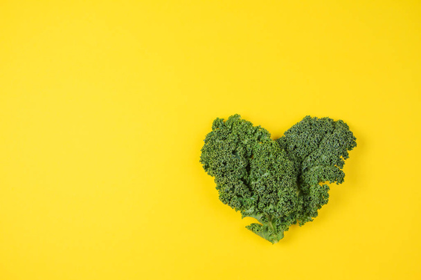 Fresh kale leaves in the shape of a heart on yellow background. - Photo, Image