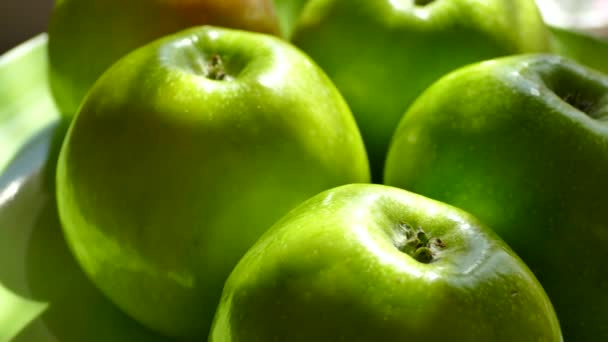 Beautiful green apples stand on a plate. A green fruit turns in front of the camera close-up. The harvest of apples and natural vitamins by nature. The girl takes the apple by hand. - Imágenes, Vídeo
