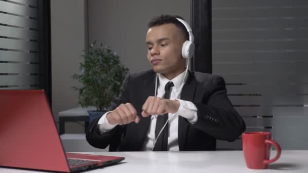 Young successful African businessman in suit listening to music on the computer in headphones, dancing in the office. 60 fps - Video