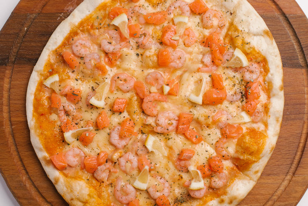 Близький погляд на піцу з томатним соусом, сиром, креветками, шматочками лосося та лимона, які подаються на дерев'яній тарілці для піци
  - Фото, зображення
