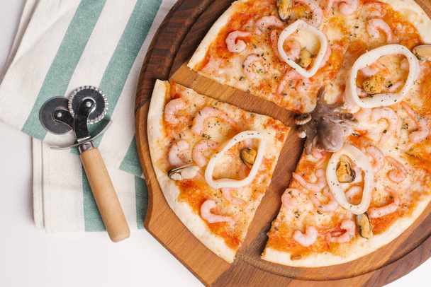 Gros plan de pizza tranchée avec sauce tomate, fromage, poulpe, anneaux de calmar et moules servis sur une assiette de pizza en bois avec coupe-pizza et serviette
 - Photo, image