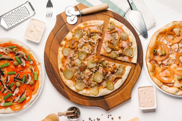 Trzy rodzaje pizzy serwowane na biały stół z sosami, serwetka i przybory kuchenne - Zdjęcie, obraz