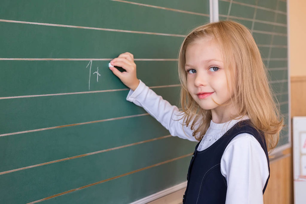 Eerste rang leerling een meisje op school les op groene schoolbord schrijven - Foto, afbeelding