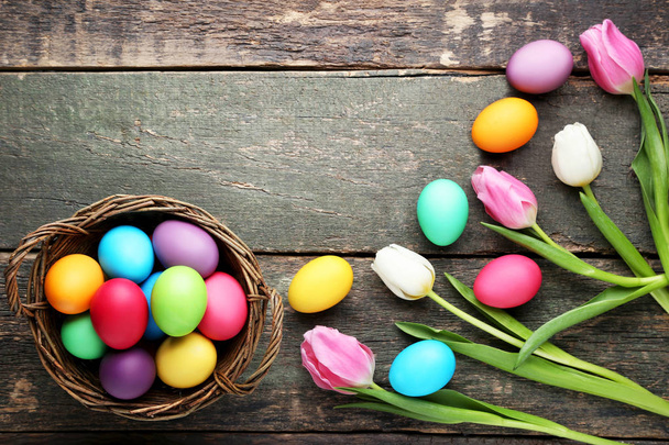 Colorful easter eggs in basket with tulips on wooden table - Fotografie, Obrázek
