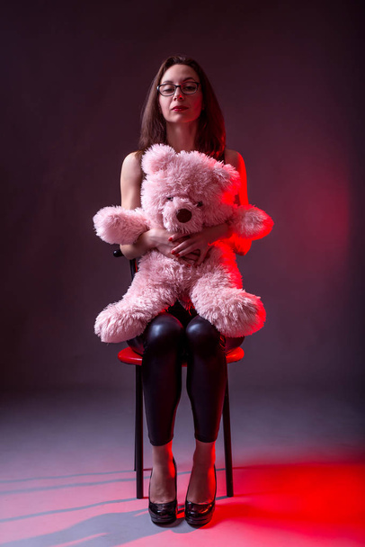 Young woman sitting on a chair and holding a pink bear. - Fotografie, Obrázek