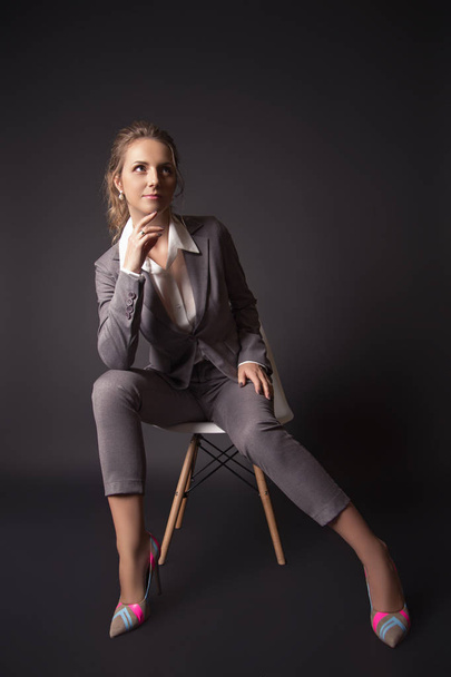 business lady in suit  sits on a chair on black background - Foto, Bild