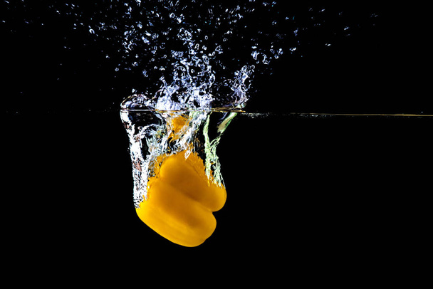 Fresh yellow paprika in water splashes on a black background. - Foto, imagen