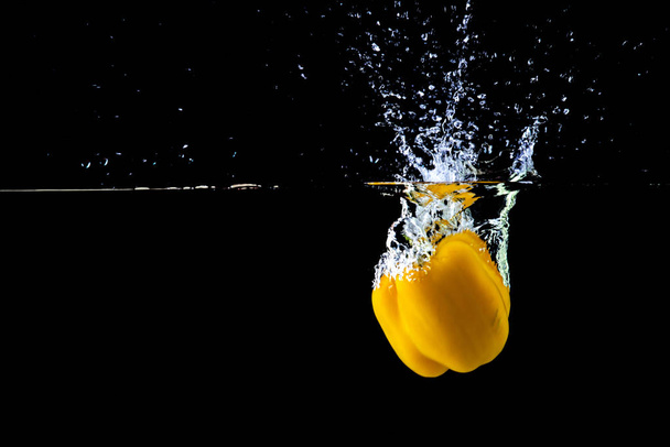 Fresh yellow paprika in water splashes on a black background. - Fotografie, Obrázek