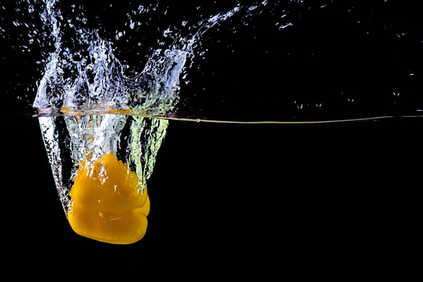Fresh yellow paprika in water splashes on a black background. - Фото, изображение