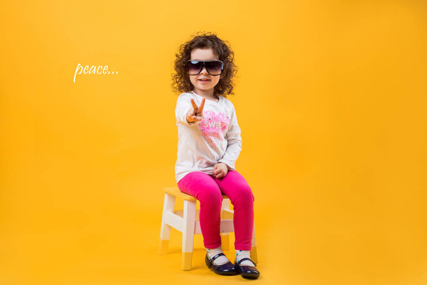 Little girl shows two fingers, gesture of peace on a yellow background - Fotoğraf, Görsel