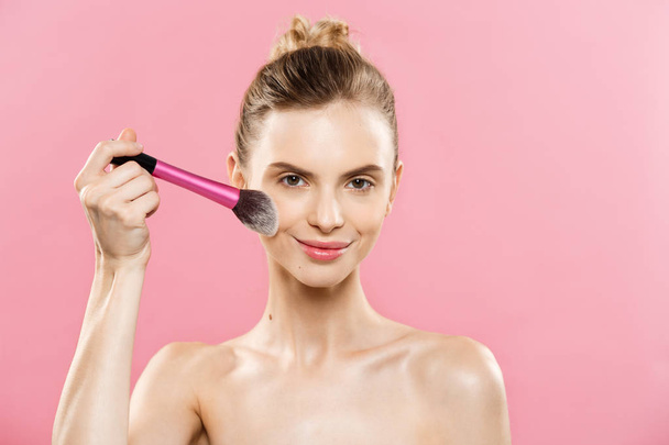 Beauty Concept - close-up mooie Kaukasische vrouw toepassing van make-up met cosmetische poeder borstel. Perfecte huid. Geïsoleerd op roze achtergrond en kopie ruimte. - Foto, afbeelding