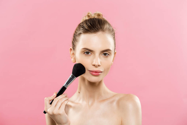 Ομορφιά έννοια - όμορφη Closeup καυκάσιος γυναίκα εφαρμογή μακιγιάζ με καλλυντικά βούρτσα σκόνης. Τέλειο δέρμα. Απομονωμένα σε ροζ φόντο και αντίγραφο χώρου. - Φωτογραφία, εικόνα