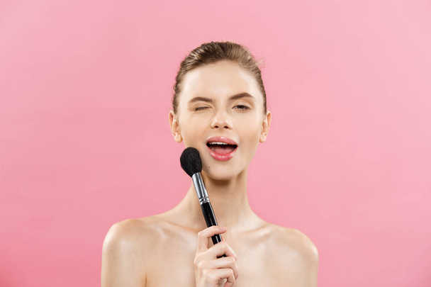 Beauty Concept - Closeup Beautiful caucasian woman applying makeup with Cosmetic Powder Brush. Perfect Skin. Isolated on pink background and copy space. - Foto, imagen