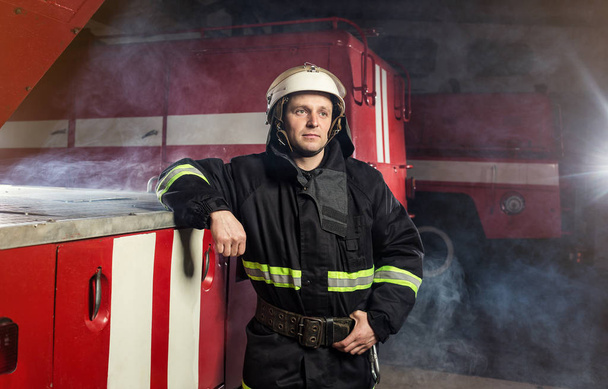 Brandweerman (brandweerman) in actie staande in de buurt van een brandweerwagen. De veiligheid van de noodsituatie. Bescherming, redding van gevaar. - Foto, afbeelding