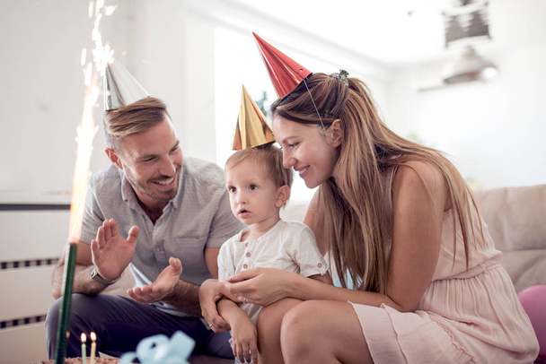 Γιορτή, οικογένεια, διακοπές και γενέθλια έννοια-ευτυχής οικογένεια με παιδί καπέλα και κέικ στο σπίτι. - Φωτογραφία, εικόνα