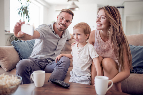 Happy couple with boy taking selfie while sitting on couch at home. - Photo, Image