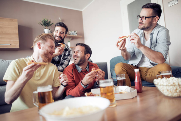 Čtyři muži přátelé sledování televize doma, zatímco jíst pizzu a pít pivo. - Fotografie, Obrázek