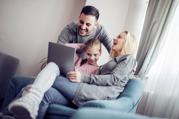 Happy parents with daughter using laptop in living room. - Foto, Imagem