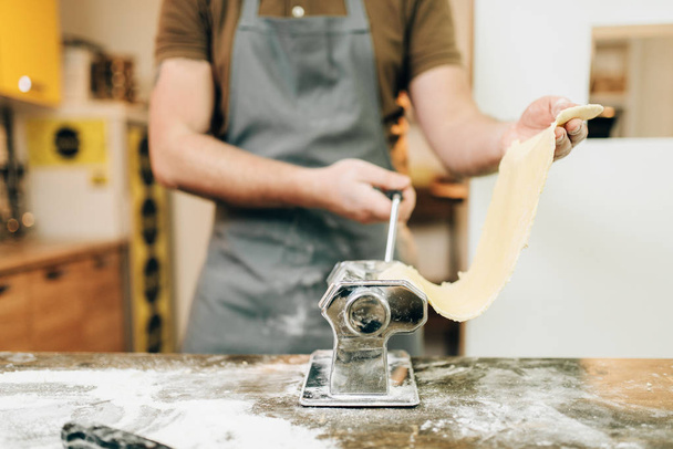 chef in apron working with dough from pasta machine on wooden kitchen table - Foto, immagini