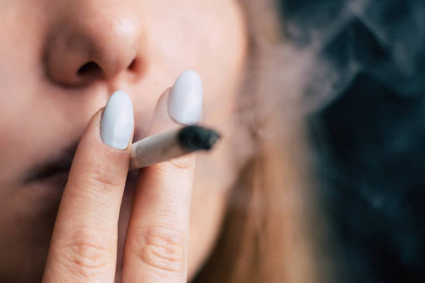 Женщина курит марихуану, косяк и зажигалку в его руках. Дым на черном фоне. Концепции использования медицинской марихуаны и легализации марихуаны
. - Фото, изображение